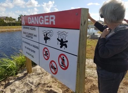 Resident Alice Finst on bank of LWDD canal looking at danger sign.