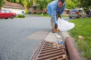 man picking up trash from storm drain