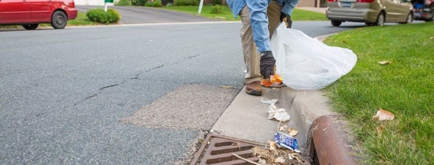 man picking up trash from storm drain