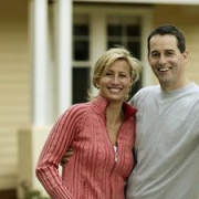 Couple in front of home leaning on fence